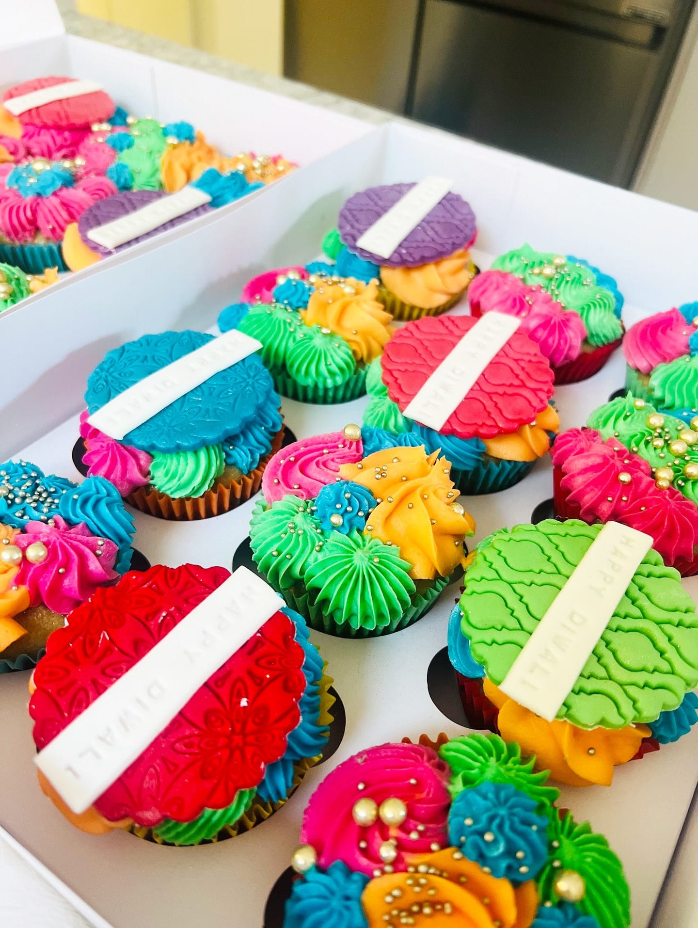 Box of brightly coloured party cupcakes piped in pink, blue, green and orange buttercream