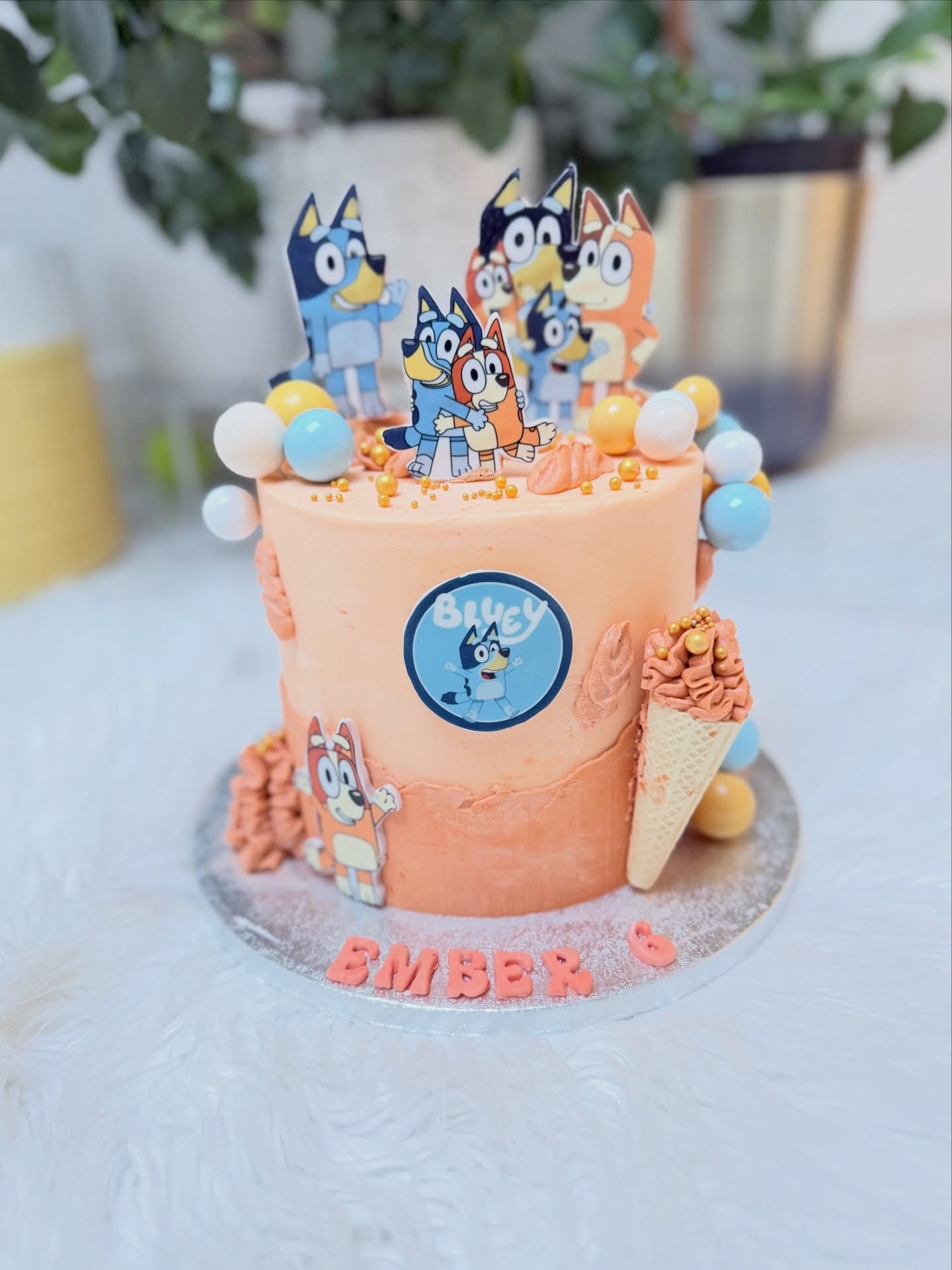 Peach buttercream children's birthday cake with pastel and gold bubbles, an ice cream cone and character toppers