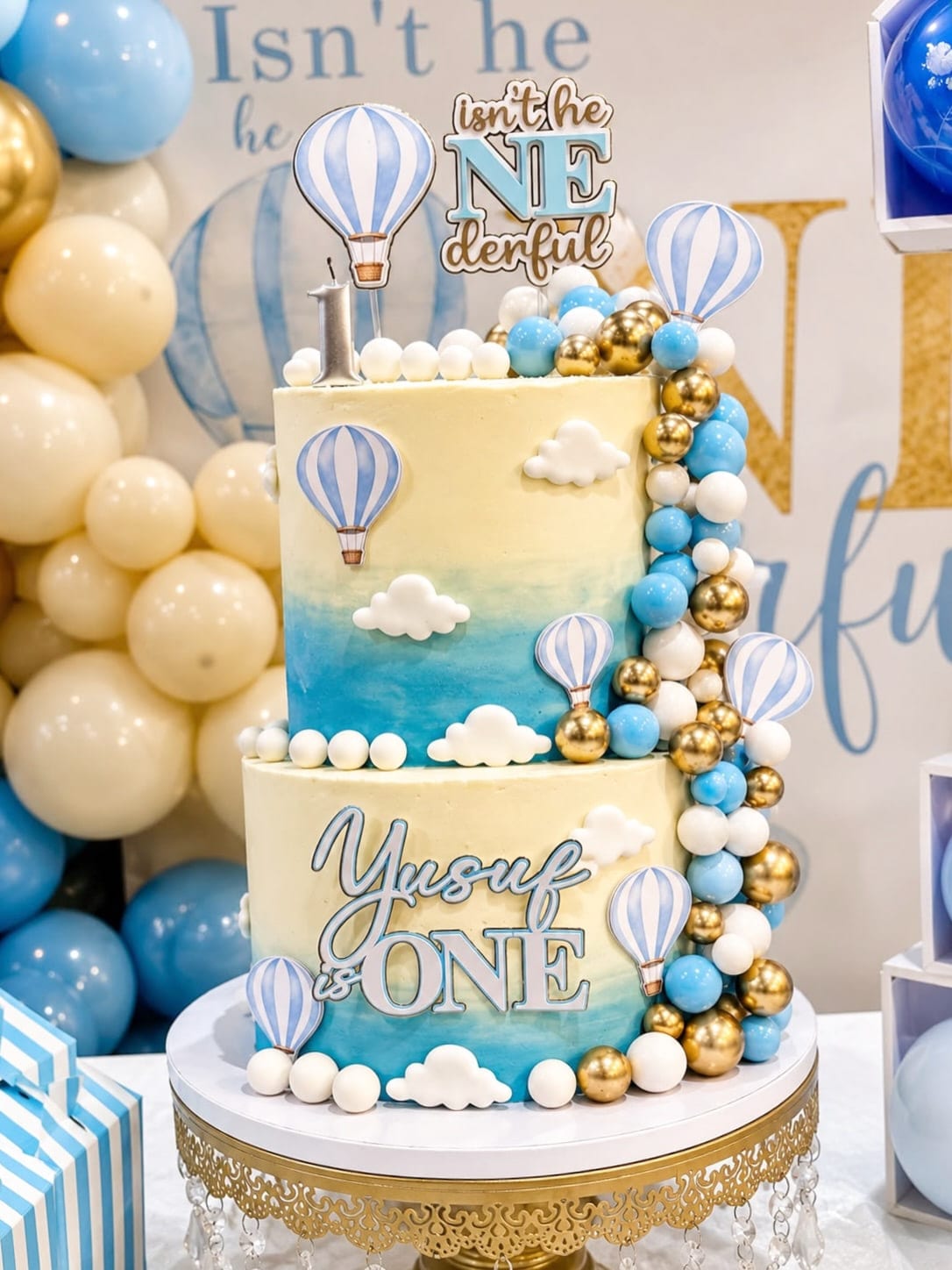 Two-tier first birthday cake with a painted sky, fondant clouds and hot air balloons in blue and gold