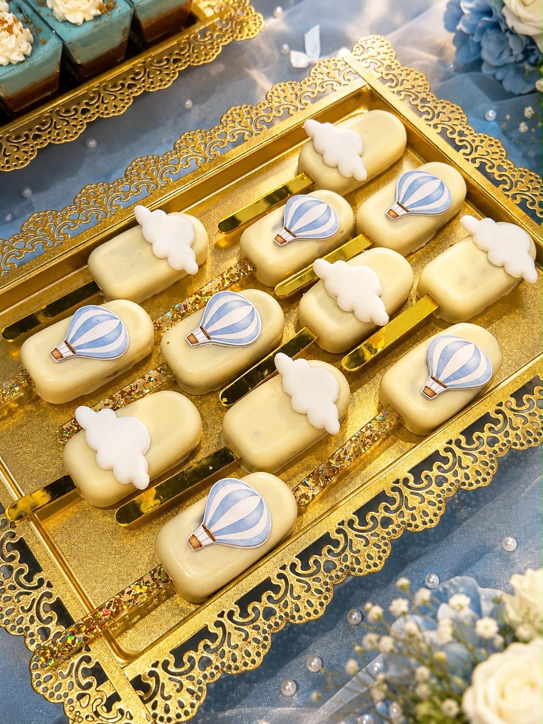 Individual dessert bites topped with fondant hot air balloons and clouds on a gold tray