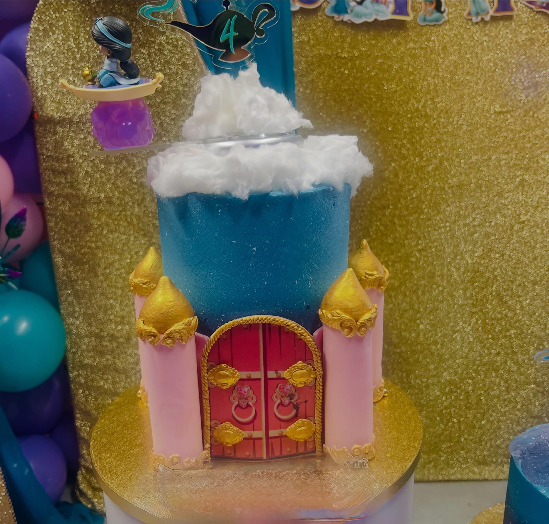 Sculpted princess castle birthday cake with gold turrets, pink doors and a spun cloud top