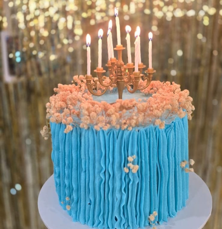Tall blue ruffled buttercream celebration cake topped with peach blossom and a candelabra