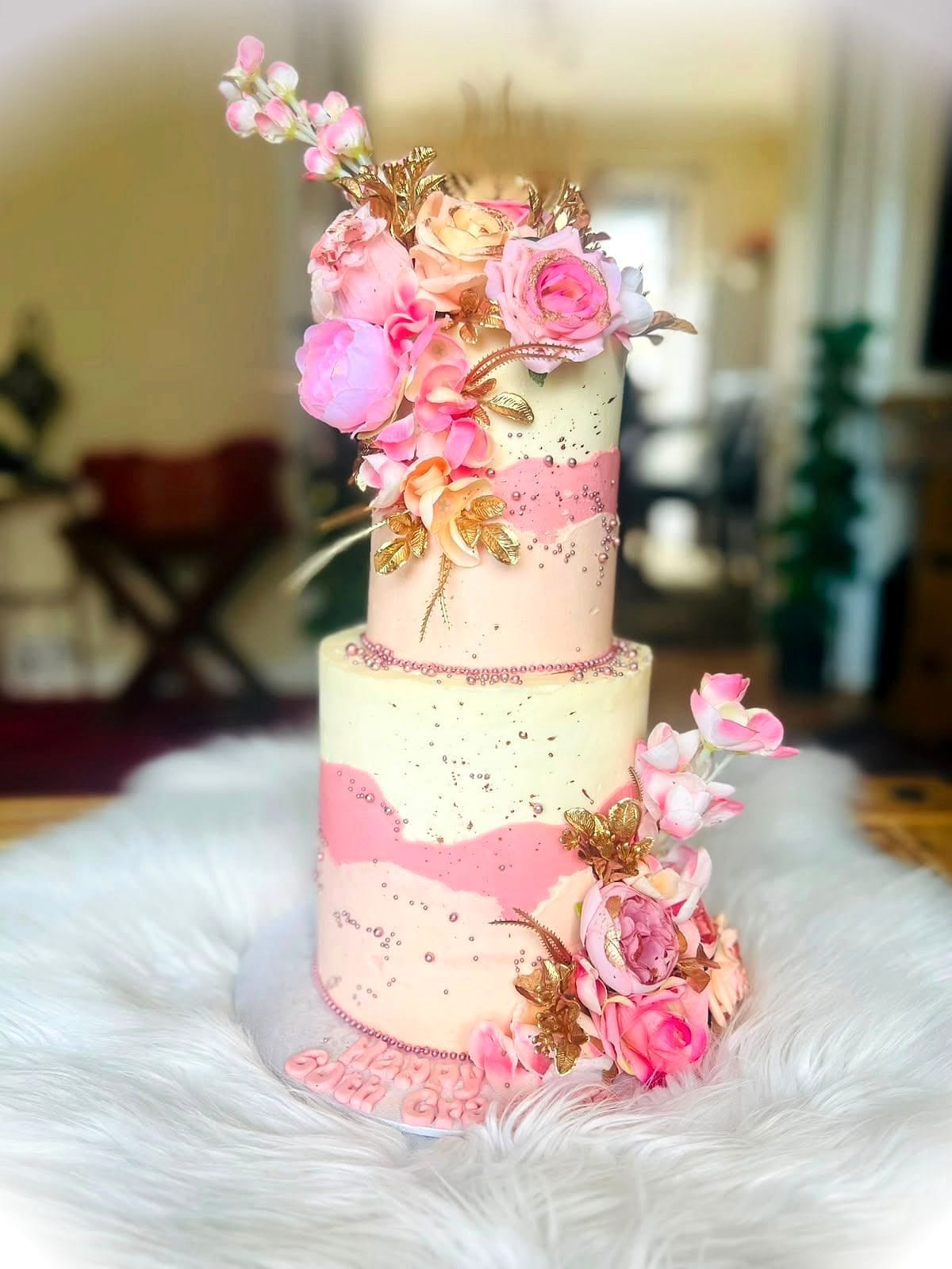 Blush Floral Two-Tier Cake by SpongyBakes — A two-tier blush and cream cake with gold flecks and a cascading floral spray.