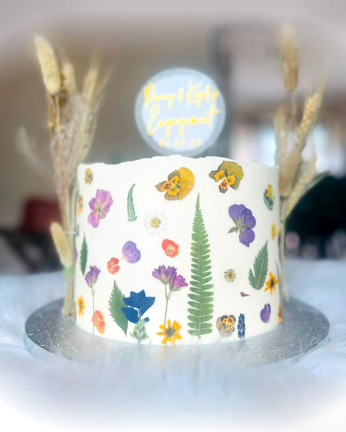 Wildflower Meadow Cake by SpongyBakes — A white buttercream cake scattered with pressed wildflowers and dried grasses.