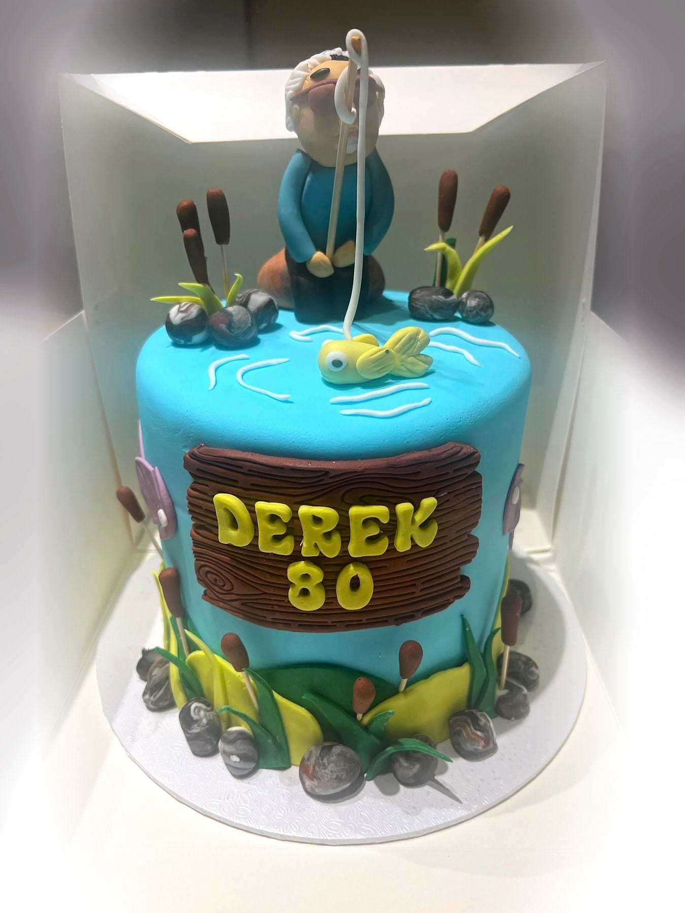 Fishing Milestone Cake by SpongyBakes — A lakeside cake with a hand-modelled angler, bulrushes and a carved name plaque.