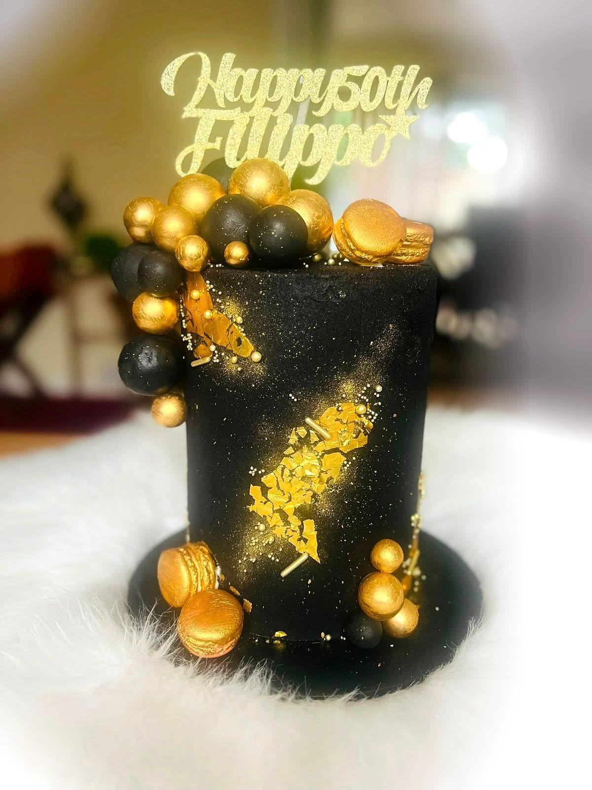 Black & Gold 50th Birthday Cake by SpongyBakes — A black cake with gold leaf, a chocolate sphere cluster, macarons and a gold topper.